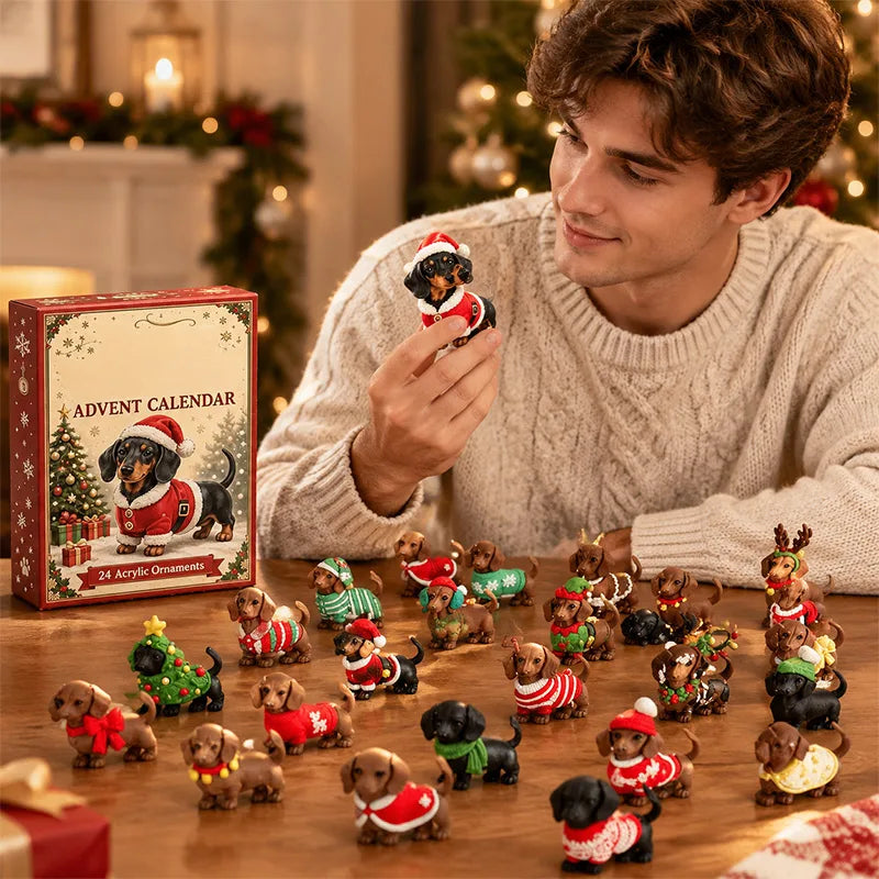 A man in a cream knit sweater holds a small dachshund Christmas ornament while surrounded by many similar dachshund figurines in holiday outfits on a wooden table. A boxed advent calendar labeled 'ADVENT CALENDAR' and '12 Advent Christmas' sits beside him in a warmly lit holiday room.